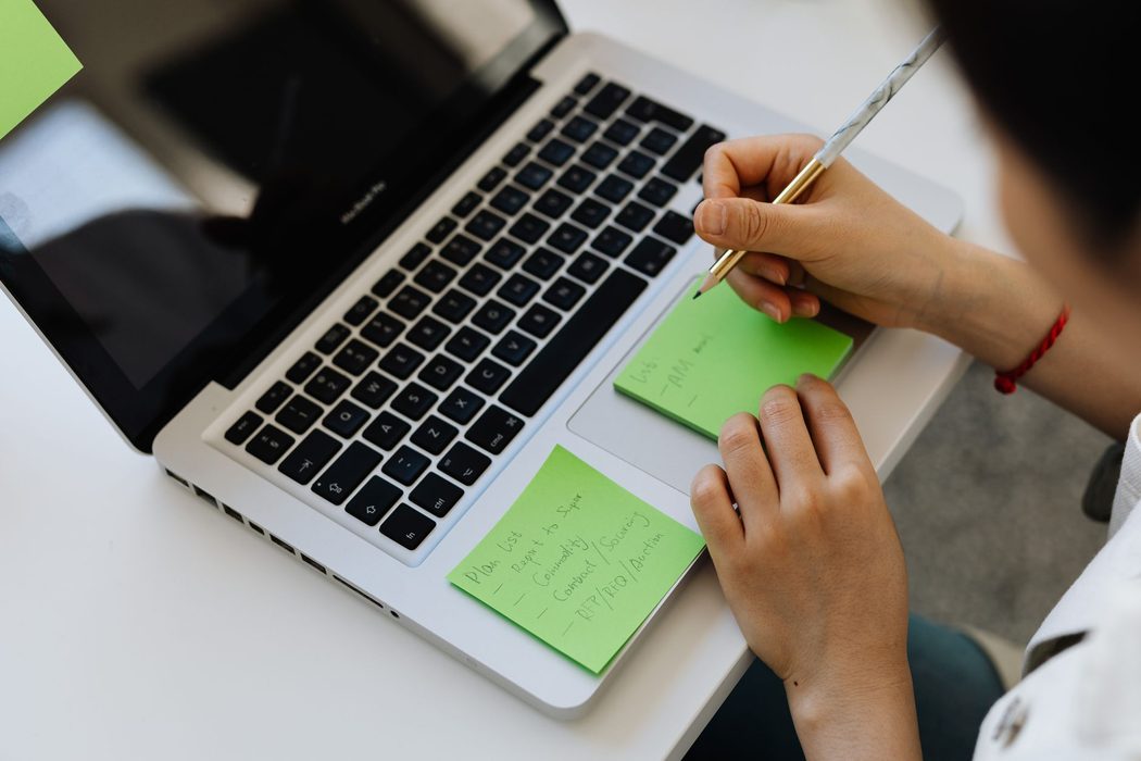 A person taking notes beside a laptop while researching a topic